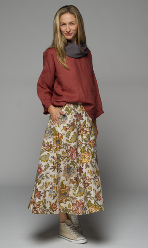 A women wearing a grey scarf on a long sleeve rust coloured top and floral skirt.