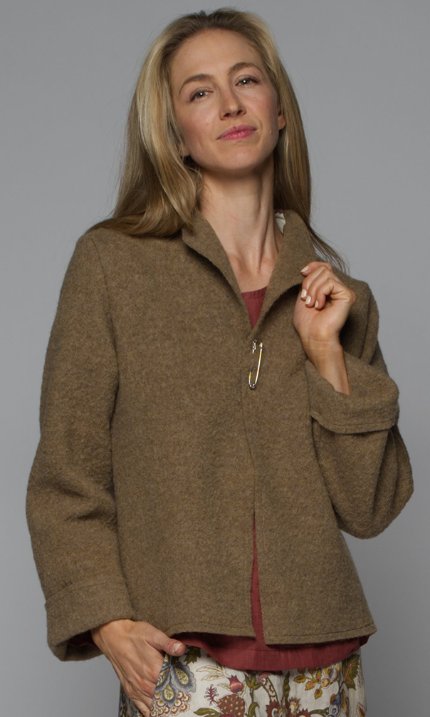 A woman wearing a brown v-neck jacket with a red top and floral skirt.