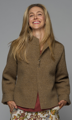 A woman wearing a brown v-neck jacket with a red top and floral skirt.
