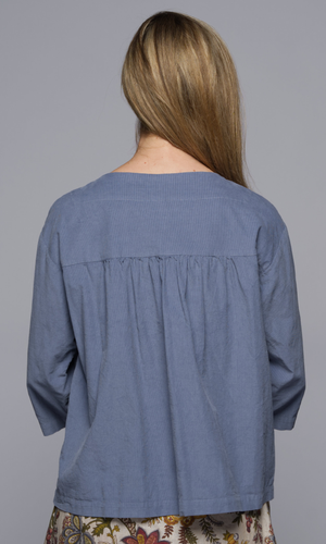 A woman wearing a blue shirt, showing us the back of the garment.