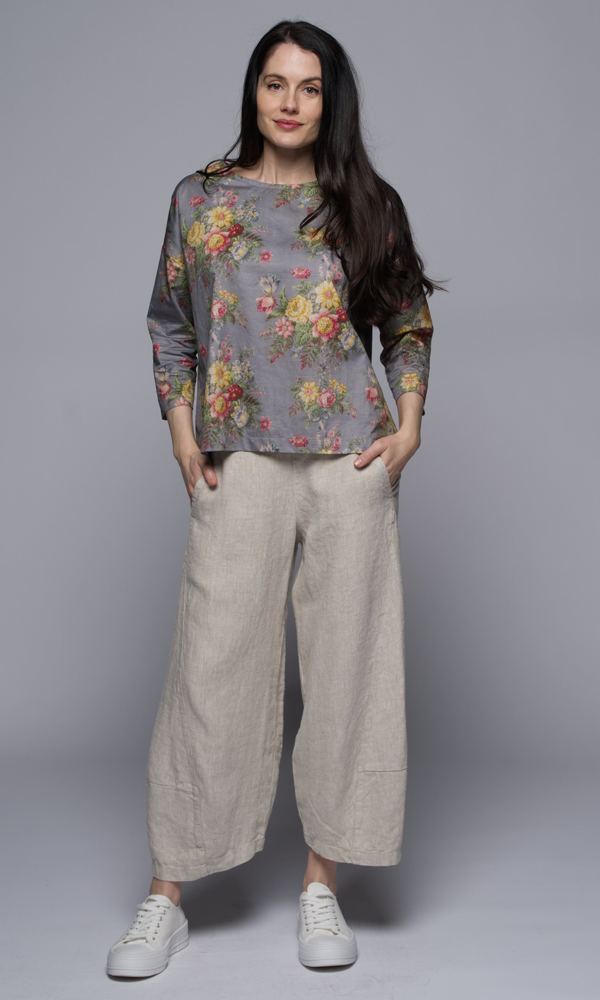 A woman wearing a floral top with light beige linen pants.