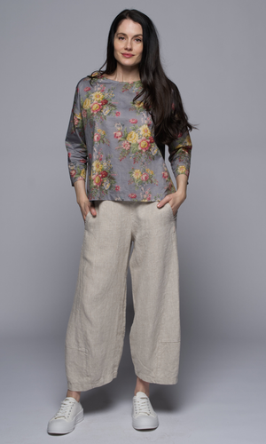 A woman wearing a floral top with light beige linen pants.