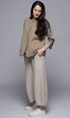 A woman wearing a beige jacket and pants, her hand in her pocket, in profile.