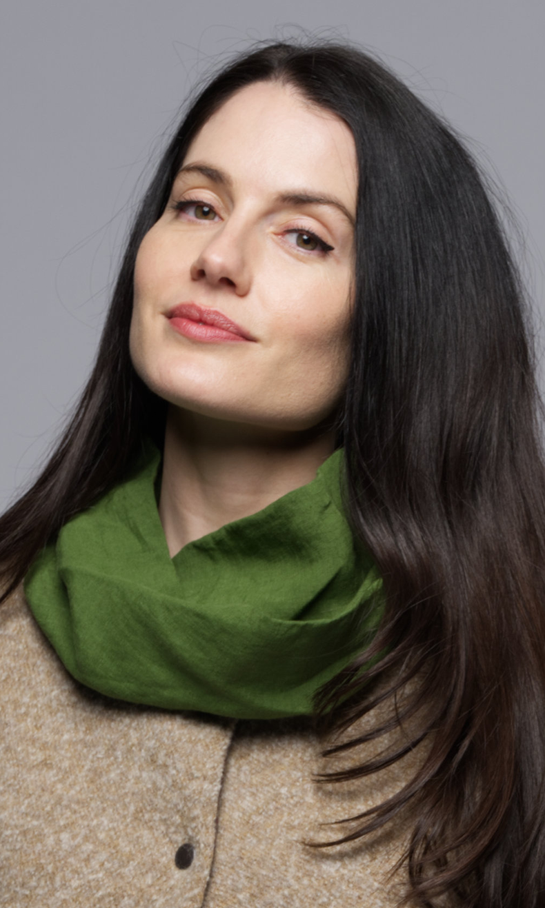 A women wearing a green scarf on a beige vest with a floral top.