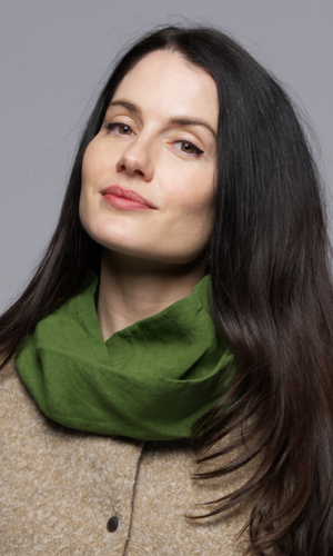 A women wearing a green scarf on a beige vest with a floral top.