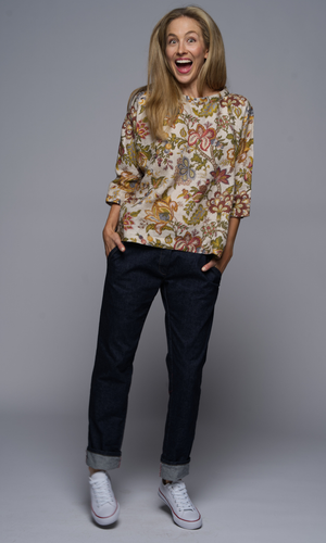 Woman wearing a floral blouse and denim blue jeans, with white sneakers.