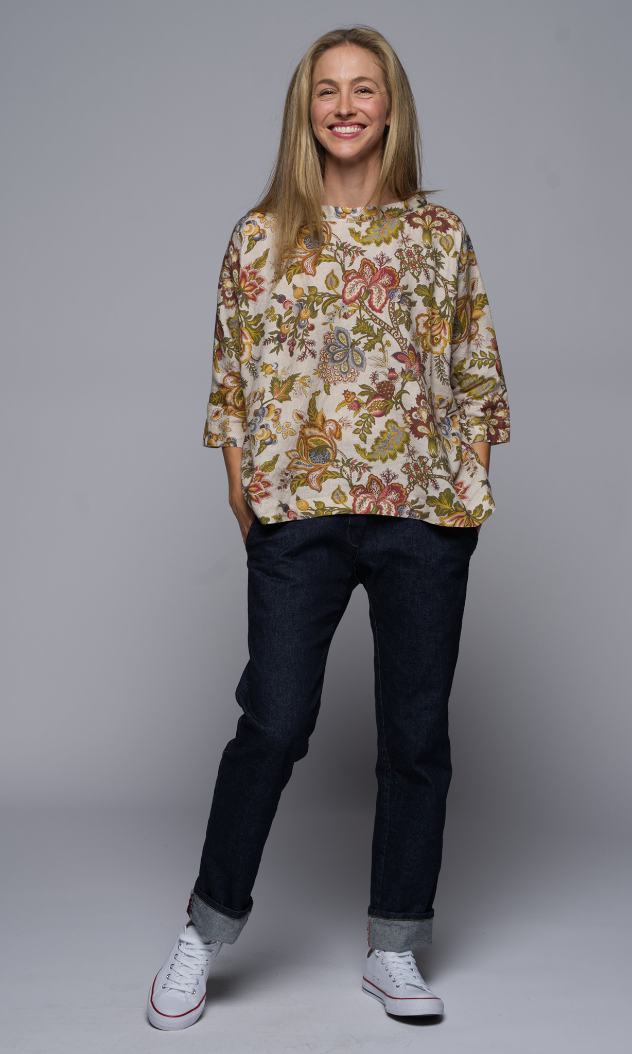 Woman wearing a floral blouse and denim blue jeans, with white sneakers.