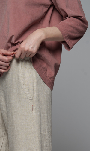 A close up of a woman's hand wearing a pink long sleeved top with a natural cream coloured pants.