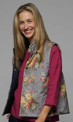 A woman wearing a floral vest with a pink top and a pair of blue jeans.