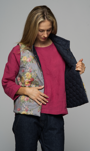 A woman wearing a floral vest with a pink top and a pair of blue jeans.