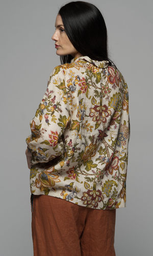 A woman wearing a long sleeve top with a floral pattern and corduroy beige pants, shows us the back of the garments.