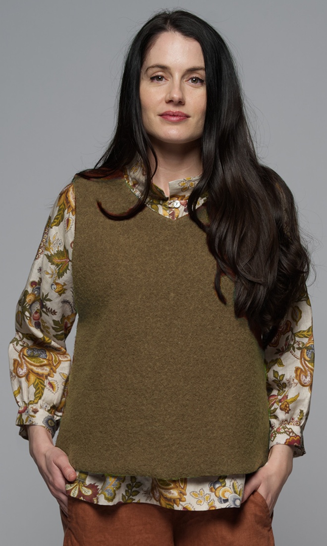 A woman wearing a beige wool vest with a floral top and rust coloured pants..