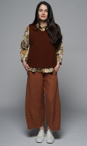 A woman wearing a brown outfit with a floral shirt, a brown vest and lighter brown pants.