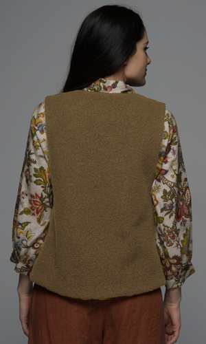 A woman wearing a beige wool vest with a floral top and rust coloured pants, showing the back of the vest.