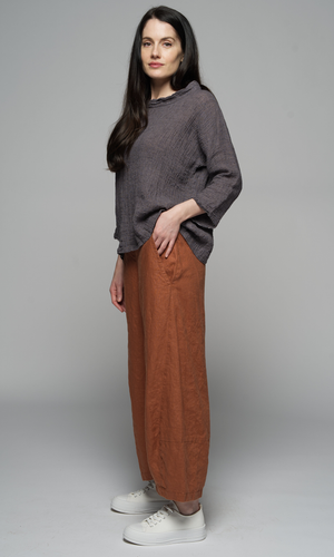 A woman wearing a grey sweater and brown pants, with her hand in her pocket, side view.