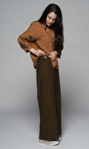 A woman wearing a brown outfit, showing off buttons on the side of her pants.