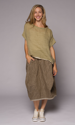 Blonde woman modelling a green linen top with a brown loose skirt, hand in pocket.