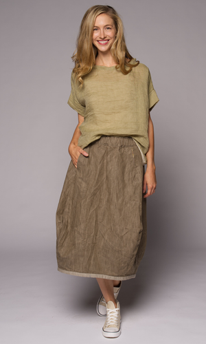 Blonde woman modelling a green linen top with a brown loose skirt, hand in pocket.