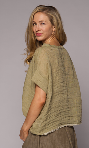 Side view of a blonde woman modelling a green linen top with a brown loose skirt.