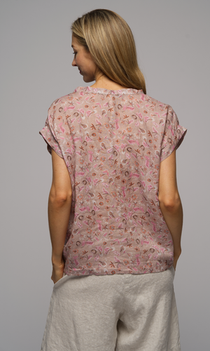 Lady wearing a short sleeve floral top with cream shorts, showing back of top.