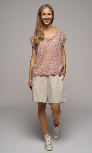 Lady wearing a short sleeve floral top with cream shorts.