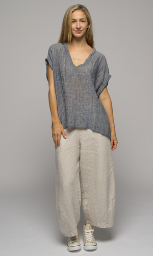 Woman wearing a blue/grey top with beige/ white linen flowing pants, facing the camera.