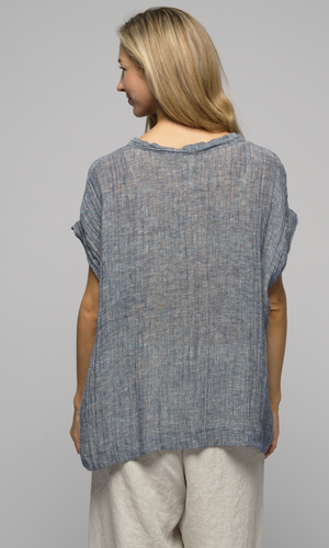 Woman wearing a blue/grey top with beige/ white linen flowing pants, showing us the back of the top.