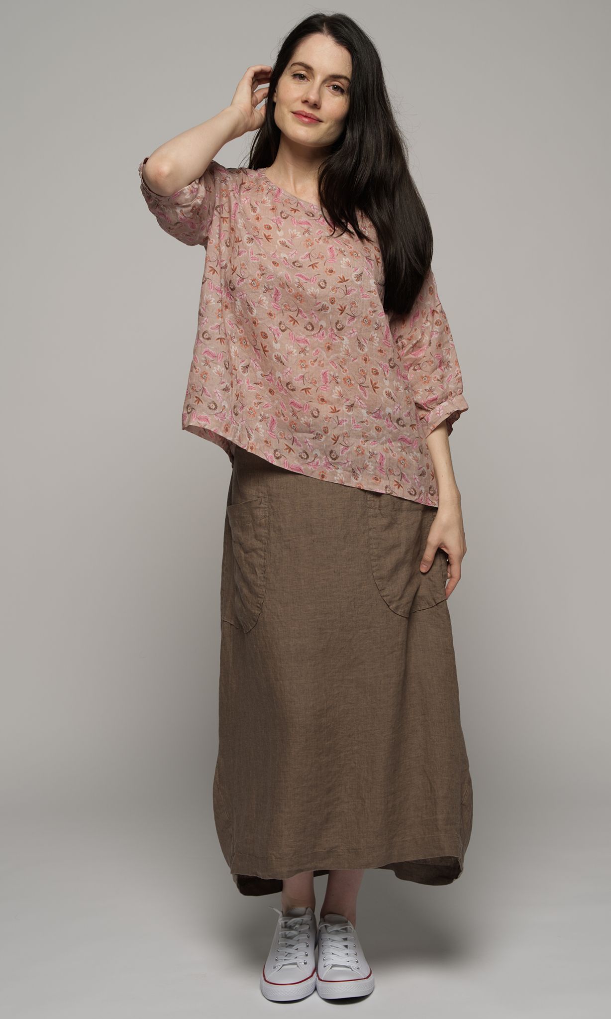 Woman wearing a elbow length floral patterned blouse with a brown skirt.