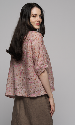 Woman wearing a elbow length floral patterned blouse with a brown skirt, showing you the back of the garments.