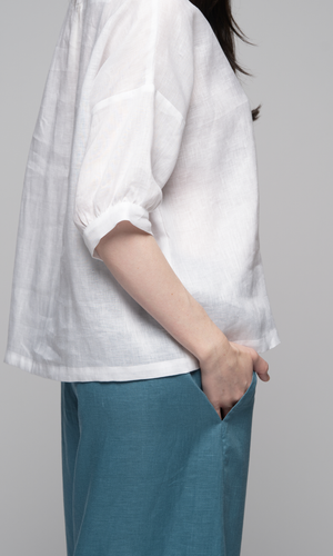 Lady wearing a white top with sleeves to elbows and a teal blue coloured pants, showing pocket detail on pants.