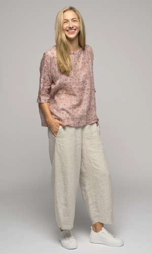 Lady in a pink floral elbow length top wearing white or cream coloured pants.
