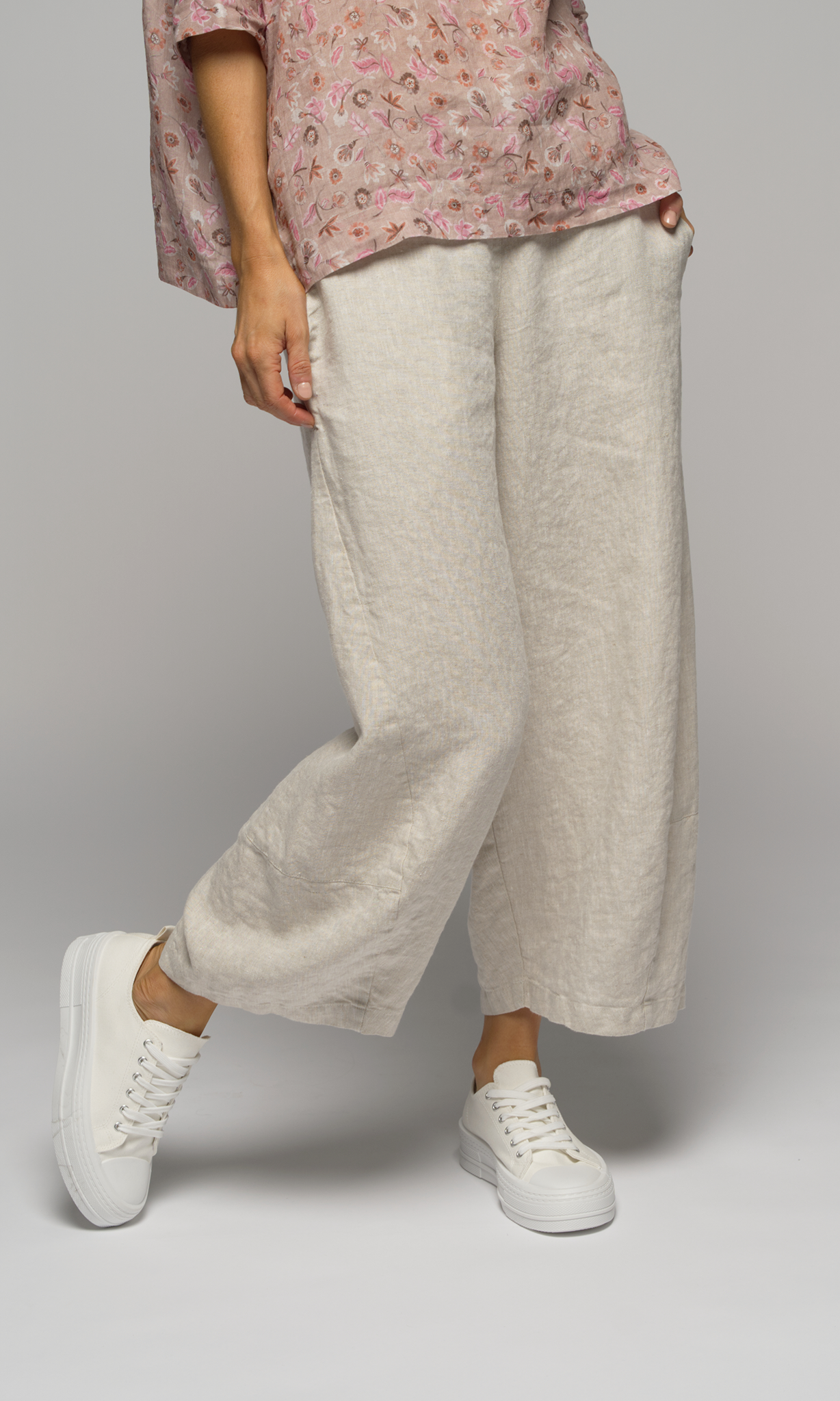Lady in a pink floral elbow length top wearing white or cream coloured pants, showing a closeup of the pants.