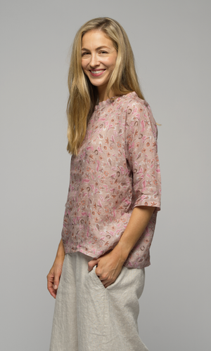 Lady in a pink floral elbow length top wearing white or cream coloured pants showing a closeup of the top.