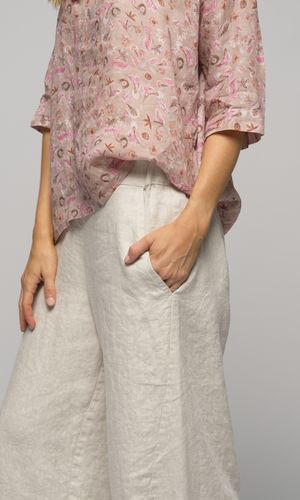 Lady in a pink floral elbow length top wearing white or cream coloured pants, showing the pocket detail of the pants.
