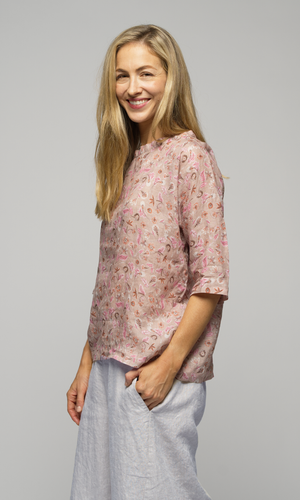 Lady wearing a floral 3/4 sleeve blouse with white ankle length pants, showing pocket detail on pants.