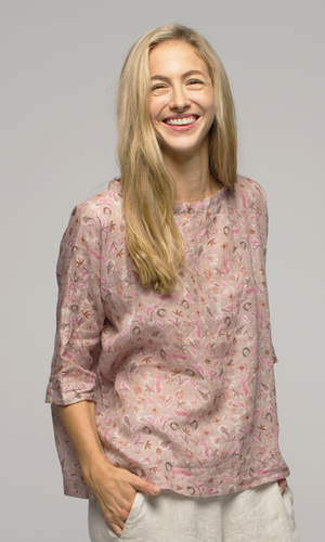Close up of a lady in a pink floral elbow length top wearing white or cream coloured pants.
