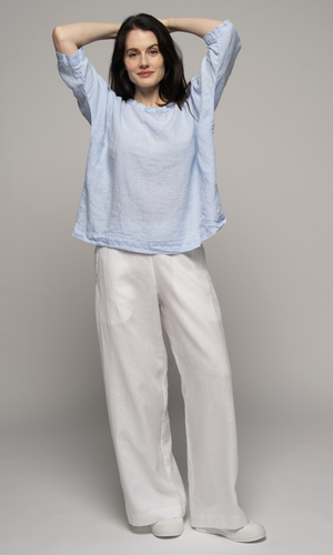 Woman wearing a light blue top and white pants, arms crossed above her head.