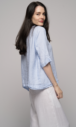 Woman wearing a light blue top and white pants turned to the right.