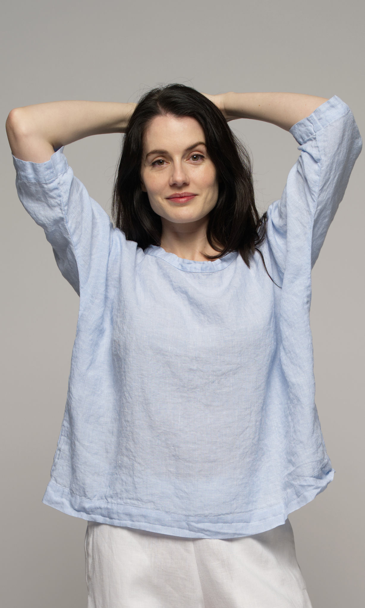 Closeup of a woman wearing a light blue top and white pants.