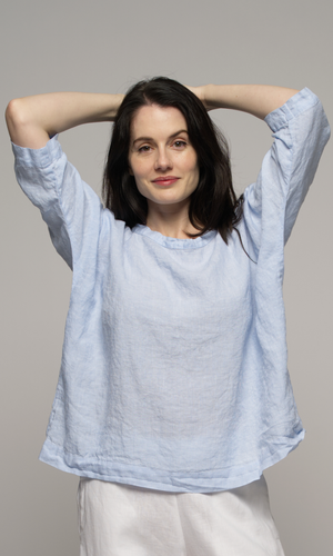 Closeup of a woman wearing a light blue top and white pants.