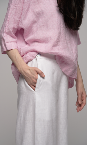 Woman wearing a pink top and white pants, showing pocket detail on pant.