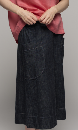 Lady wearing pink top with denim blue past knee length skirt, showing pocket detail.