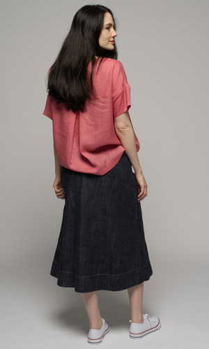Lady wearing pink top with denim blue past knee length skirt, showing back of garments.