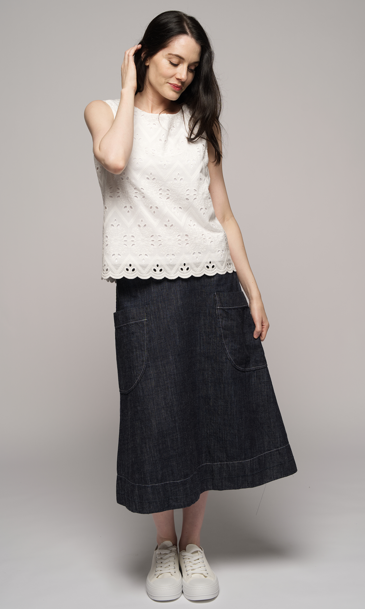 Lady wearing white sleeveless top with denim blue past knee length skirt.