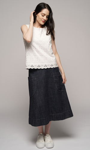 Lady wearing white sleeveless top with denim blue past knee length skirt.
