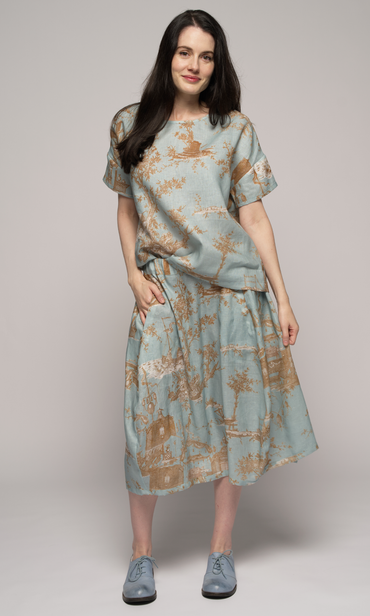 Woman wearing a light blue floral top and skirt, facing you.