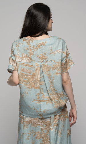 Woman wearing a light blue floral top and skirt, showing you the back of the shirt.