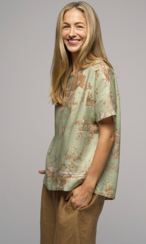 Close up of the side of a woman wearing a light green patterned shirt and light brown pants.