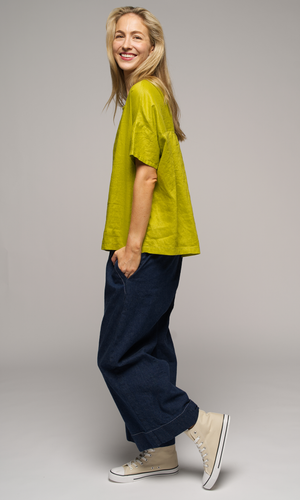 Woman wearing a greenish yellow shirt with blue denim pants, facing to the left.