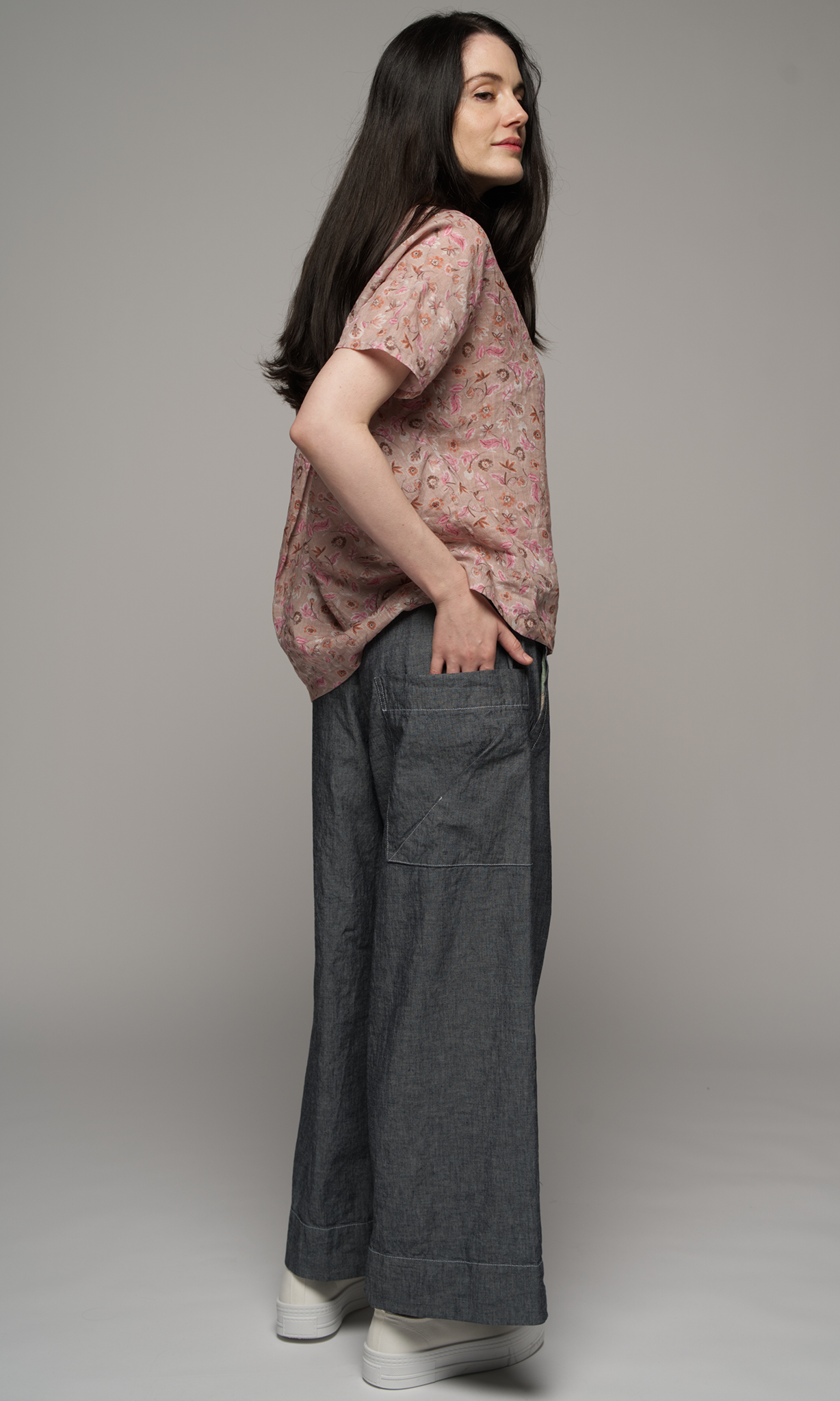 Women wearing a pink floral blouse with medium grey full length pants, showing you the back of the pants.